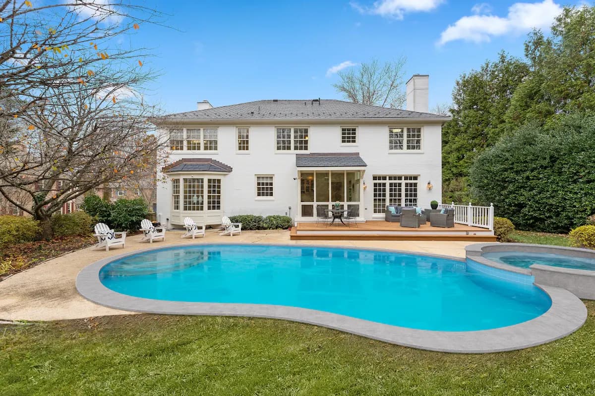 Kidney-shaped pool with an attached spa beside a lawn and house