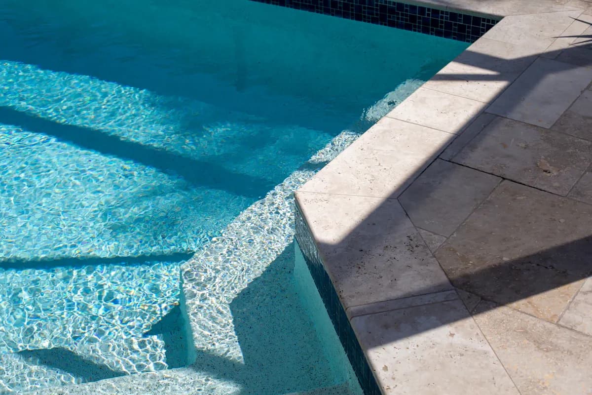 Pool steps with mosaic tile beside pale stone coping